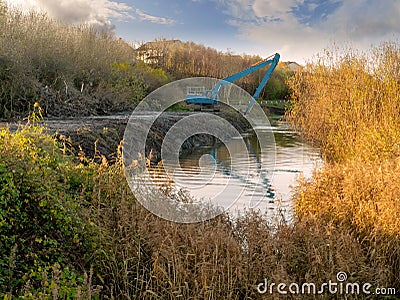 Blue excavator deepening small river, Stock Photo