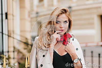 Blue-eyed female model in trendy red scarf posing with pleasure in new outfit standing beside building. Gorgeous fair Stock Photo