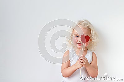 Blue eyed pretty small kid dressed casually, has fun indoors, covers eye with heart stick, glad to spend free time with Stock Photo