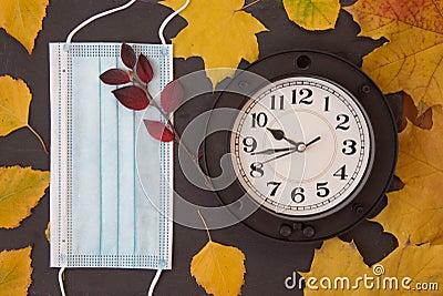 Blue face medical mask, wall clock and colorful autumn leaves. Top view Stock Photo