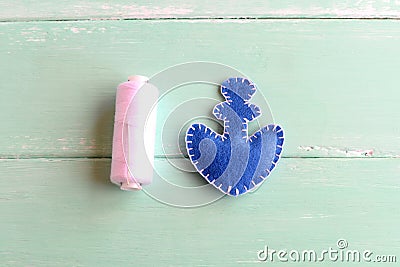 Blue felt anchor, white thread, needle on wooden background. Two pieces of felt in shape of an anchor stitched with white thread Stock Photo