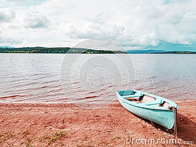 Blue fishing boat anchored on beach sand of lake. Smooth level Stock Photo