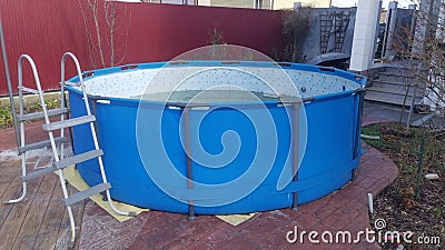 The blue frame pool is located on a paved area near the house. Nearby is the staircase and the porch of the house Stock Photo
