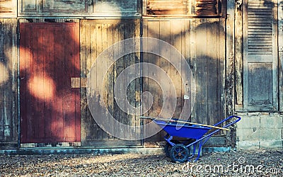 Blue garden wheelbarrow against old wooden wall Stock Photo