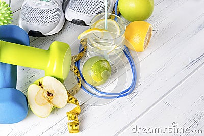 Blue and green dumbbells, a glass of water with lemon, gray sneakers, an Apple, a skipping rope, a measuring tape on a white Stock Photo