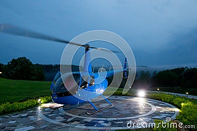 A blue helicopter is parked on a private helipad against a blue evening. Stock Photo