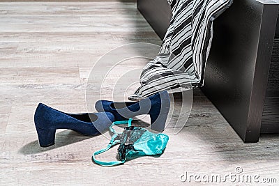 Blue high-heeled shoes, green-black lace thong panties and a condom on the wooden floor by the bed Stock Photo