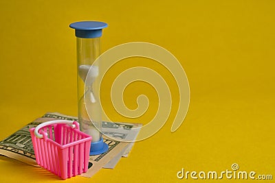 Blue hourglass and dollars with shopping basket at yellow background Stock Photo