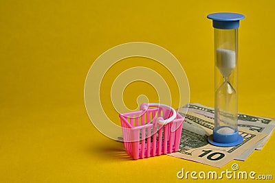 Blue hourglass and dollars with shopping basket at yellow background Stock Photo