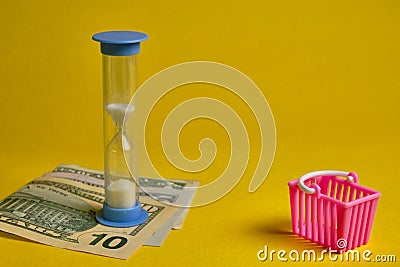 Blue hourglass and dollars with shopping basket at yellow background Stock Photo