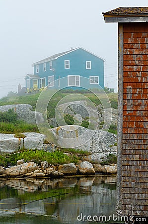 Blue House on a foggy day sitting on a rocky hill overlooking the sea and a red fishing shack Stock Photo