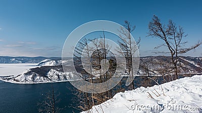 The blue ice-free Angara River flows between the snow-covered banks. Stock Photo