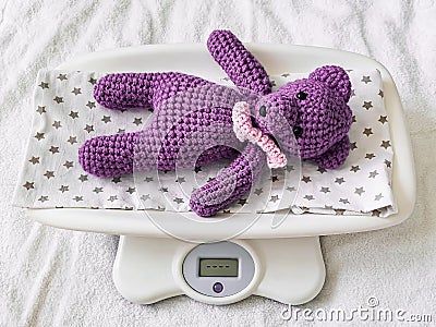 A blue knitted teddy bear lies on an electronic baby scale on a diaper with asterisks Stock Photo