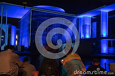 Blue light effects of buildings beyond tourists in foreground sitting looking across in Government District Berlin Editorial Stock Photo