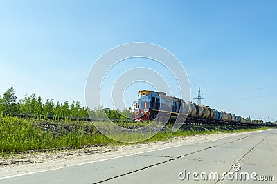 A blue locomotive tows a fuel tanks wagons against a blue sky. Stock Photo