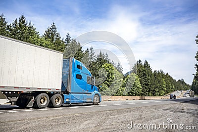 Blue long haul big rig industrial semi truck with dry van semi trailer running on the long divided highway road Stock Photo