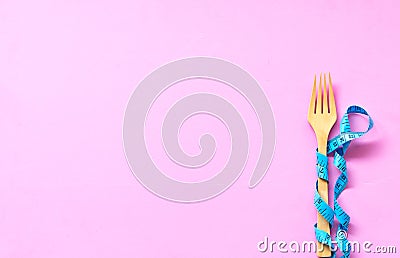 Blue Measuring tape wrapped around wood fork lying on colorful pink background. Stock Photo