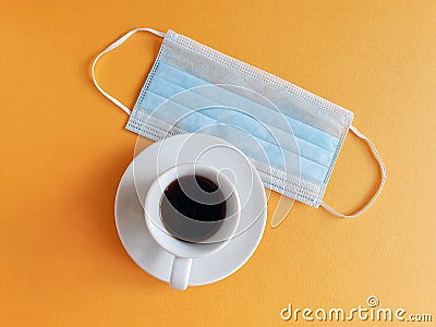 Blue medical protective mask and a cup of coffee on a yellow background. The concept of protecting your health. Stock Photo