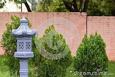 A blue medieval style lamp post for oil lamps with red brick wall and thuja plants in the background. Buddhism and spirituality Stock Photo