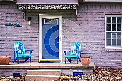 Blue mermaid adirondack chairs sit on porch of brick house painted purple with blue front door Stock Photo