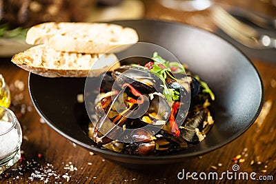 Blue mussels in white wine sauce in black bowl. Delicious healthy seafood closeup served on a table for lunch in modern Stock Photo