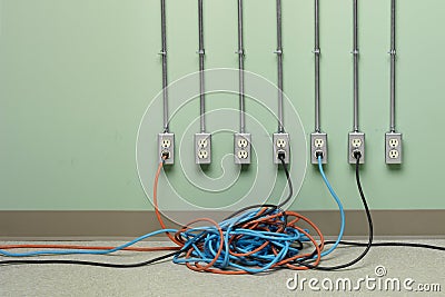 Tangled extension cords plugged into row of AC electrical outlets Stock Photo