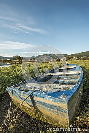 A blue painted fiberglass fishing boat hauled dry in the middle of an estuary at sunrise Stock Photo