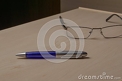 Blue pen and glasses on the office brown desk, selective focus Stock Photo