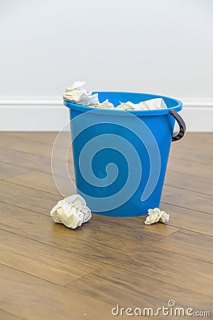 A blue plastic bucket filled with used tissues sits on a wooden floor Stock Photo