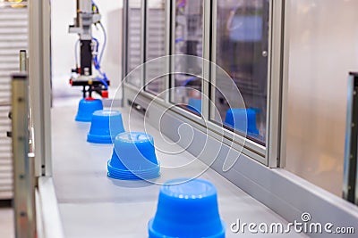 Blue pots on conveyor belt of plastic injection molding machine with robotic arm Stock Photo