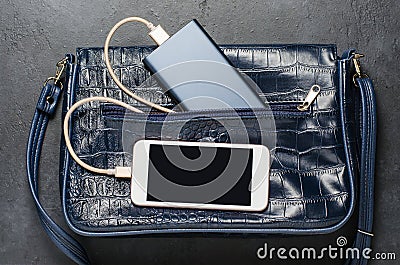 Blue Power Bank and a smartphone in the women`s bag. Dark grey concrete background Stock Photo