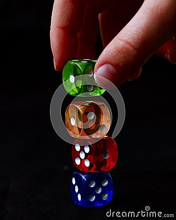 blue, red, green and yellow colored dice on top of each other and two fingers placing one Stock Photo