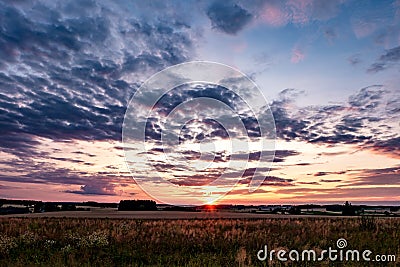 Blue red sky background with evening fluffy curly rolling clouds with setting sun. Good windy weather Stock Photo