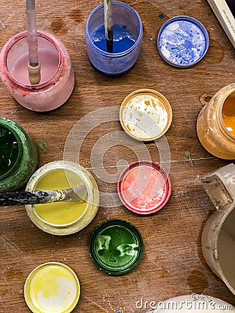 Blue, red, yellow, green pottery glaze liquid in jars with brushes on table top view in pottery studio Stock Photo