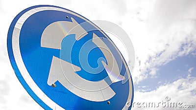 Blue road sign with arrows in a circle against sky Stock Photo