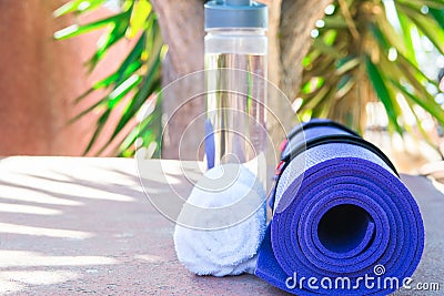 Blue Rolled Yoga Mat Bottle with Water White Towel on Greenery Palm Tree Nature Background. Sunlight. Relaxation Summer Meditation Stock Photo