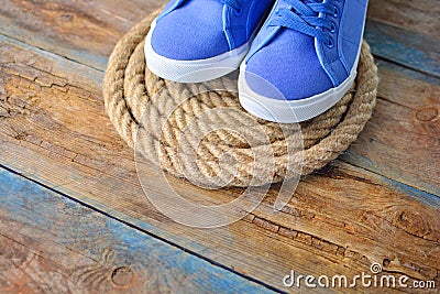 Blue sneakers shoes on a rope spiral, on a wooden weathered terrace. Yacht style concept. Stock Photo