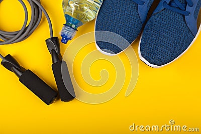 Blue sneakers, skipping rope and bottle of water on yellow background. Concept of healthy lifestile, everyday training and force Stock Photo