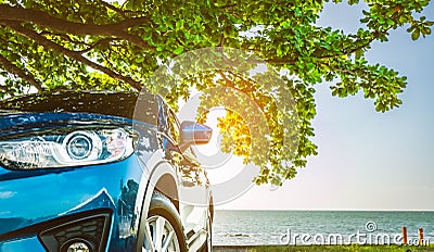 Blue sport SUV car parked by the tropical sea under umbrella tree. Summer vacation at the beach. Summer travel by car. Road trip. Stock Photo