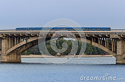 The blue subway train rides along the bridge over the river Stock Photo