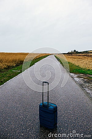 Blue suitcase on an empty field road Stock Photo