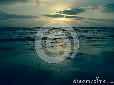 Blue sunset under a cloudy sky on a sandy beach with reflections on the wet sand. Stock Photo