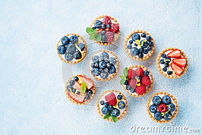 Blue table decorated of sugar powder with variety berry tartlets or cake top view. Tasty pastry desserts. Stock Photo