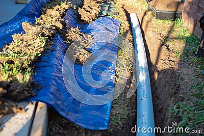 Blue tarp, black mixing tub container with dirt, underground PVC pipe buried in trench installation, rainwater drainage system Stock Photo