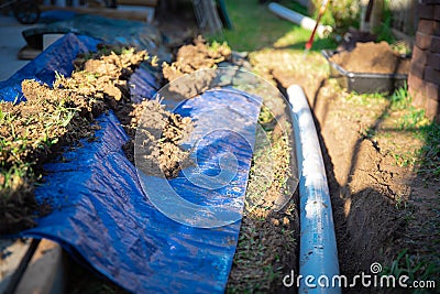 Blue tarp, black mixing tub container with dirt, underground PVC pipe buried in trench installation, rainwater drainage system Stock Photo