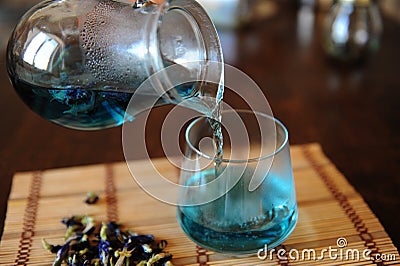 Blue Thai tea anchan is poured from jug into glass. Placer of dried flowers of clitoria tea Stock Photo