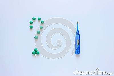 Blue thermometer on a light background. Question mark is made up of colored tablets. Stock Photo