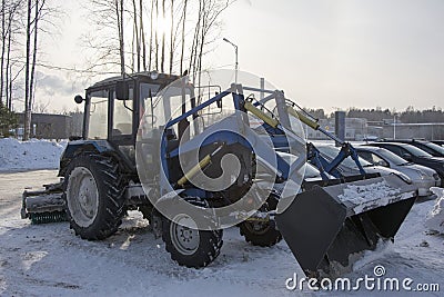 Blue tractor with a blade for snow removal in winter and a spinning brush for street cleaning Stock Photo