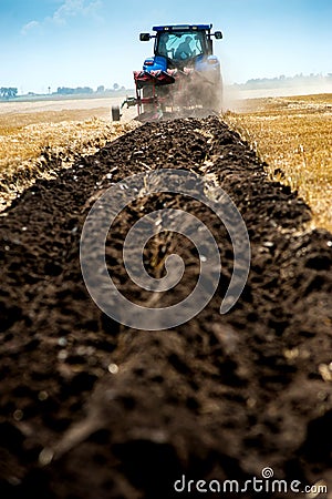 blue tractor pulls plow, tillage closeup in focus, agrarian preparing Stock Photo