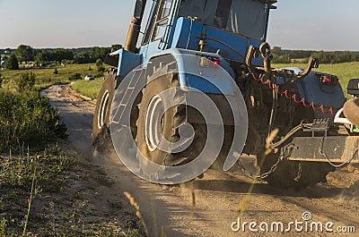 A blue tractor rides along a road in a wheat field. Stock Photo